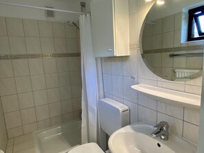 Ein Badezimmer mit Dusche, Toilette, Waschbecken und einem Spiegel darüber.