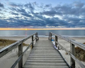 Ein hölzerner Steg führt zu einem Strand, bewölkter Himmel.