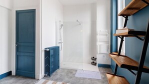 Une salle de bain avec une douche, un radiateur, une étagère en bois et une porte.