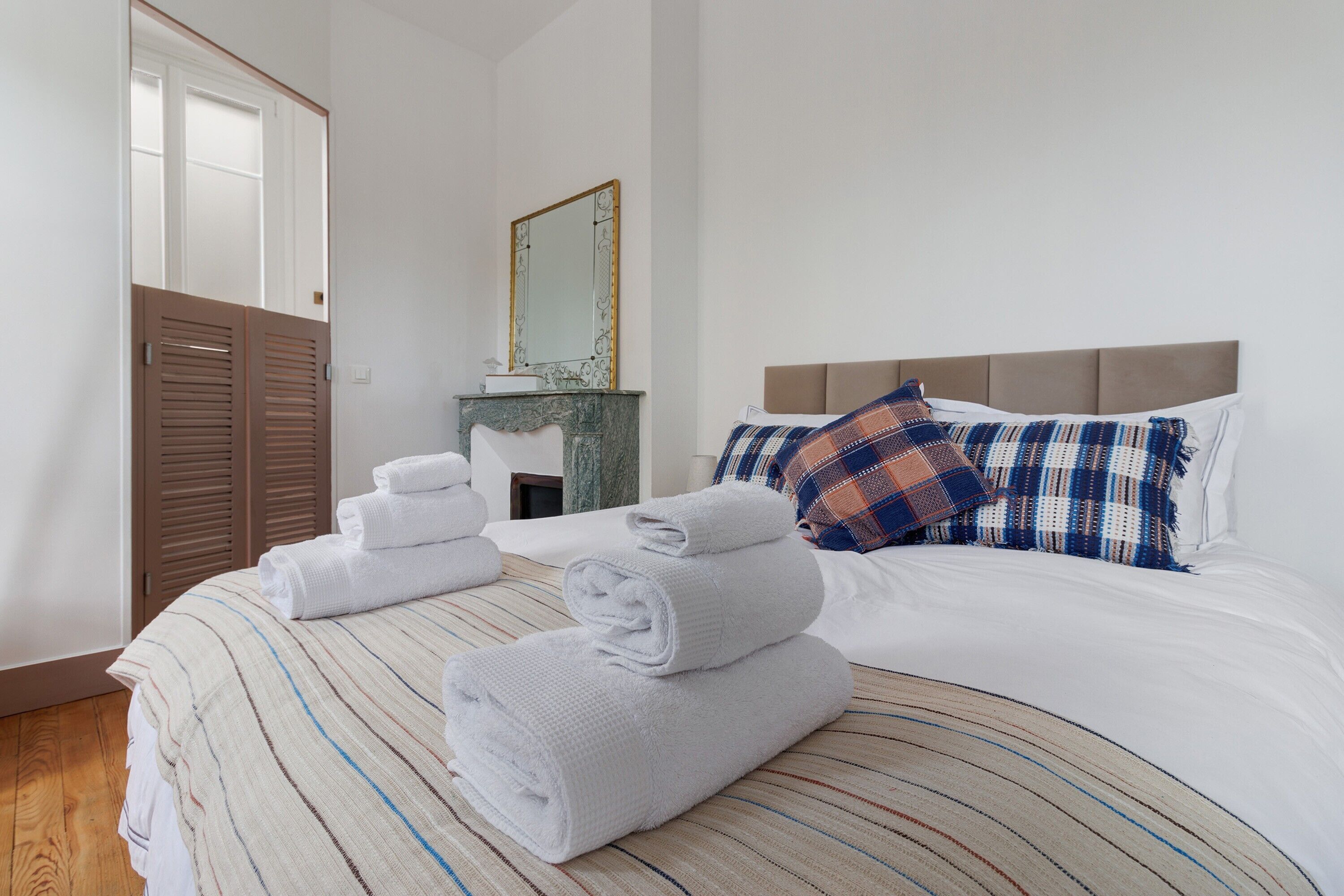 Een netjes opgemaakt bed met opgevouwen handdoeken, een hoofdbord en een geborduurde spreideken.