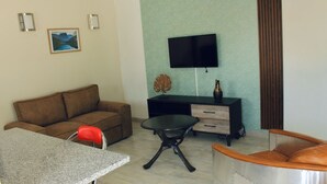 Ein Wohnzimmer mit einer Couch, einem Couchtisch, einem Fernseher, einer kleinen Kommode und einem Esstisch.