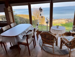 A dining area with a table and chairs, a round table with a decorative item, and a view of the sea through large windows.