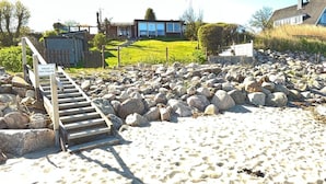 A beach with a wooden staircase leading to a private area, surrounded by large rocks and a grassy field. - fewo1846 - Haus Utkiek - fewo1846 - Utkiek / Three-bedroom vacation home (Glücksburg (Ostsee))