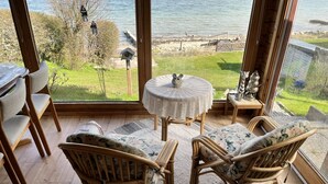A cozy room with wicker furniture, a round table, and a view of a lake. - fewo1846 - Haus Utkiek - fewo1846 - Utkiek / Three-bedroom vacation home (Glücksburg (Ostsee))