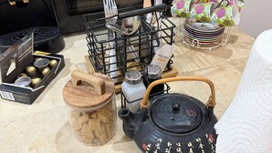 Un plan de travail de cuisine avec une machine à café, une théière, des salières et des poivrières, un présentoir à épices et une assiette décorative.