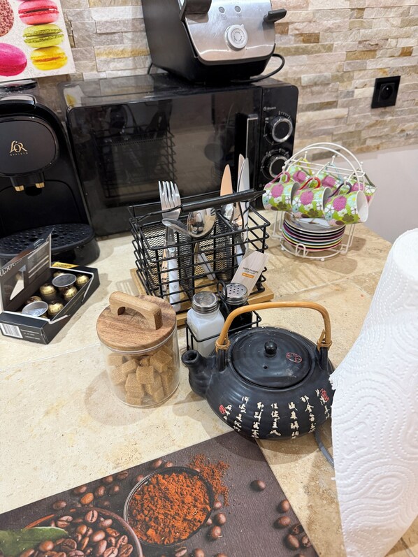 Un plan de travail de cuisine avec une machine à café, une théière, des salières et des poivrières, un présentoir à épices et une assiette décorative.