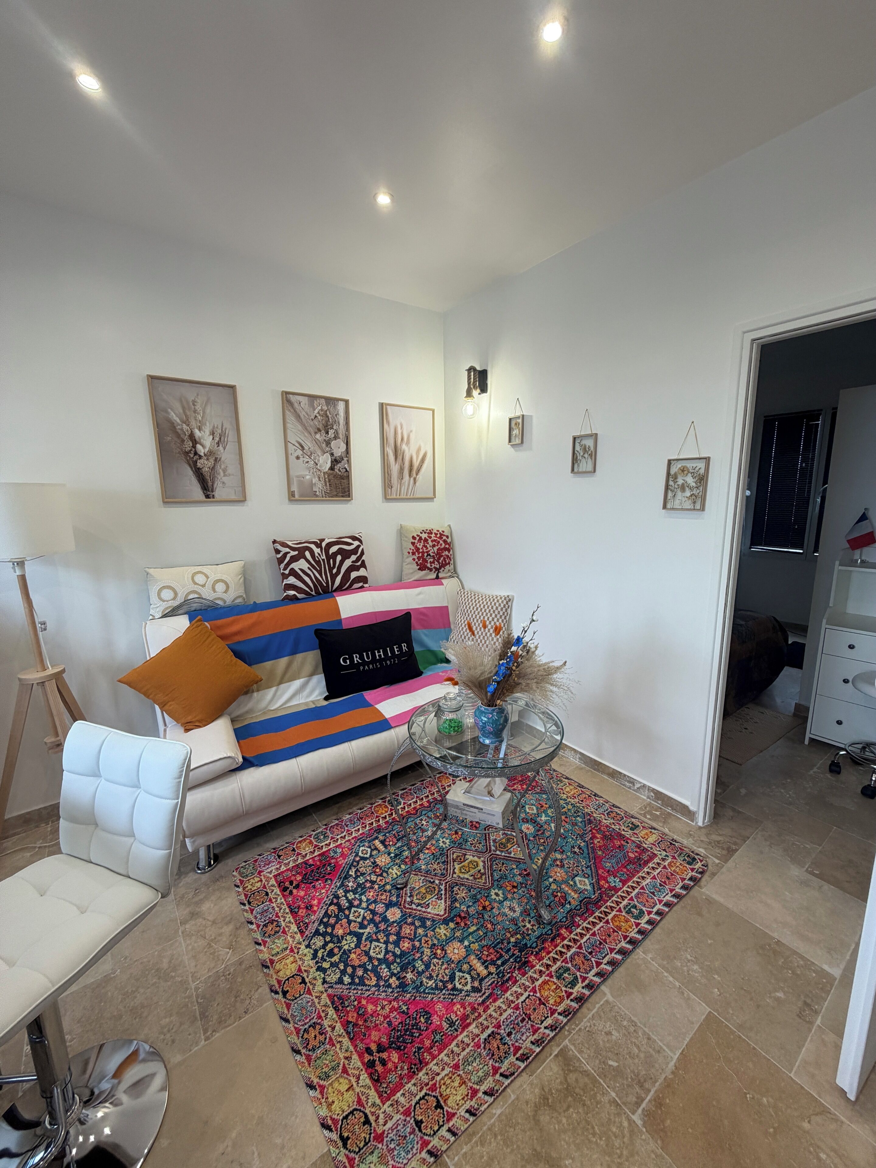 Een woonkamer met een witte bank, kleurrijke kussens, een glazen salontafel en een kamerkleed met dessin.