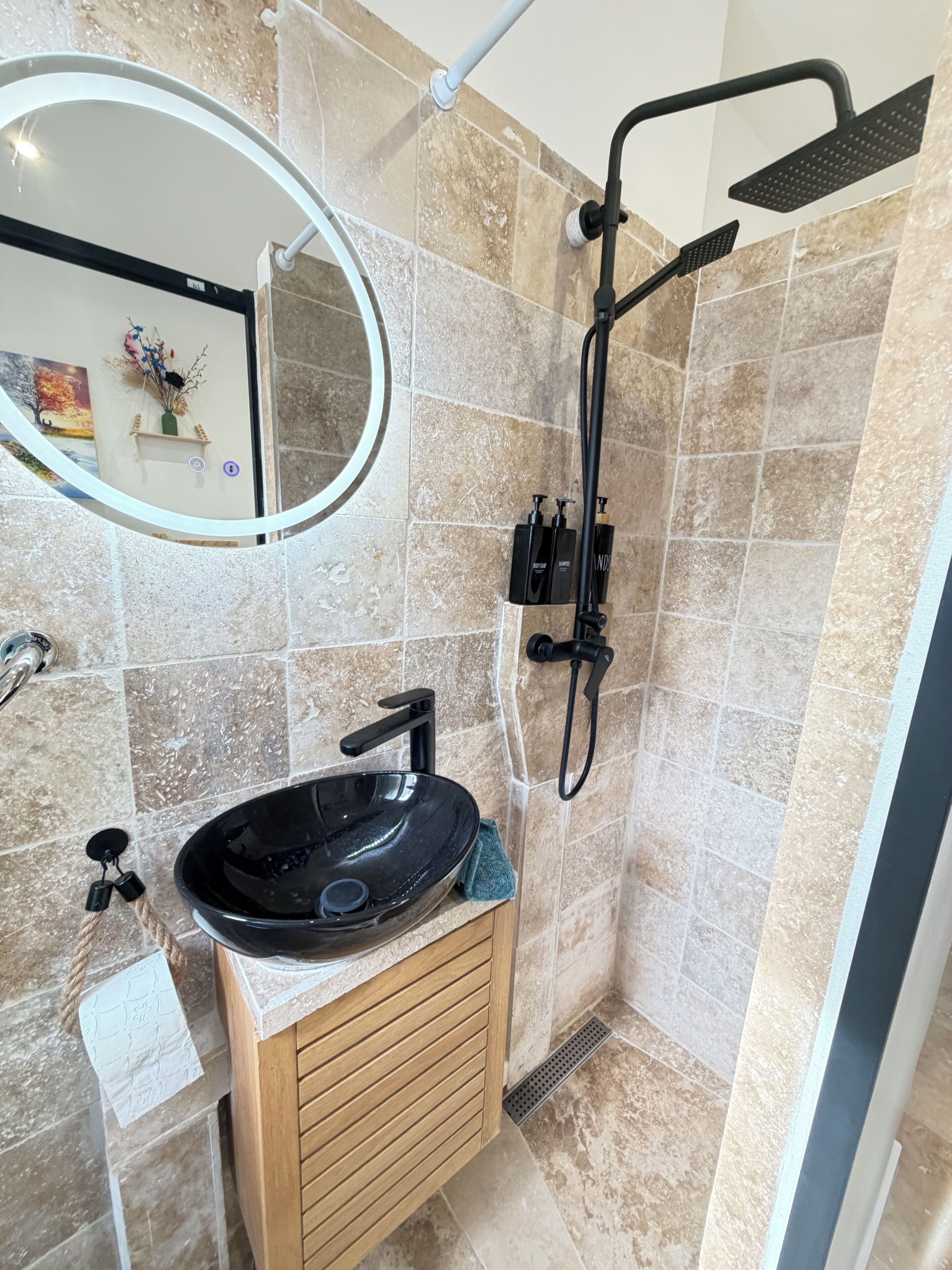 Un baño con un espejo redondo, un lavabo negro y una ducha.
