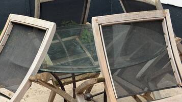 Trois chaises d’extérieur, dotées d’un dossier en tissu ajouré et d’une structure en bois, sont disposées sur une terrasse carrelée, adossées à un mur sombre.
