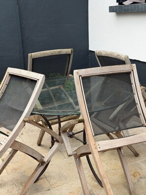 Three outdoor chairs with mesh backs and wooden frames, positioned on a tiled patio against a dark wall. - The 13 th. (Rueil-Malmaison)