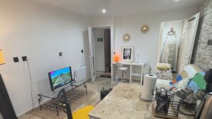 Une cuisine moderne avec un coin repas, un téléviseur et une salle de bain visible au fond.