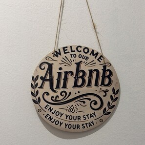 Un panneau circulaire en bois sur lequel sont inscrits les mots « Bienvenue dans notre location Airbnb » et « Passez un agréable séjour ».