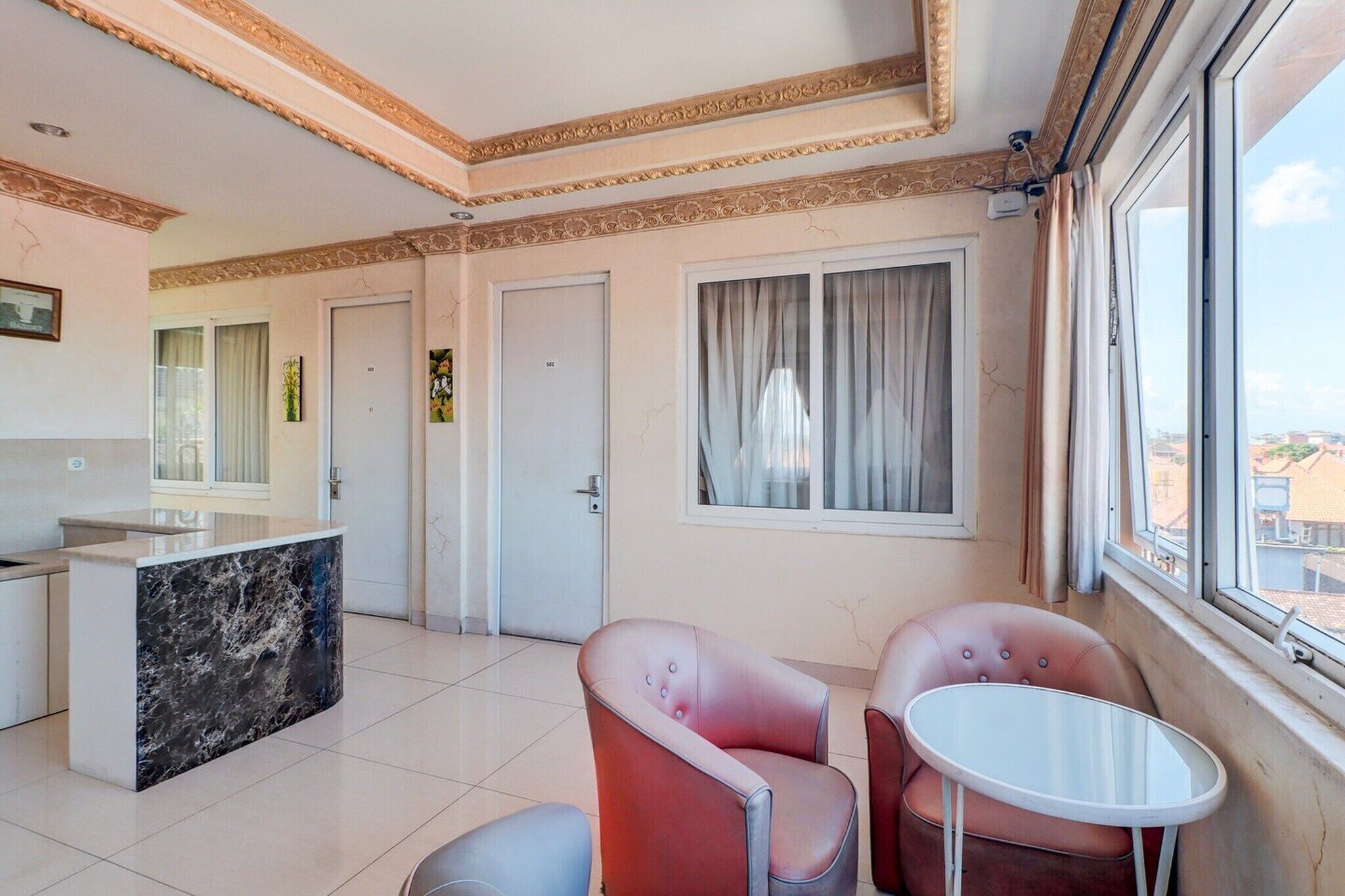 Ett hotellrum med en receptionsdisk i marmor, två rosa fåtöljer, ett litet vitt bord och ett stort fönster med gardiner.