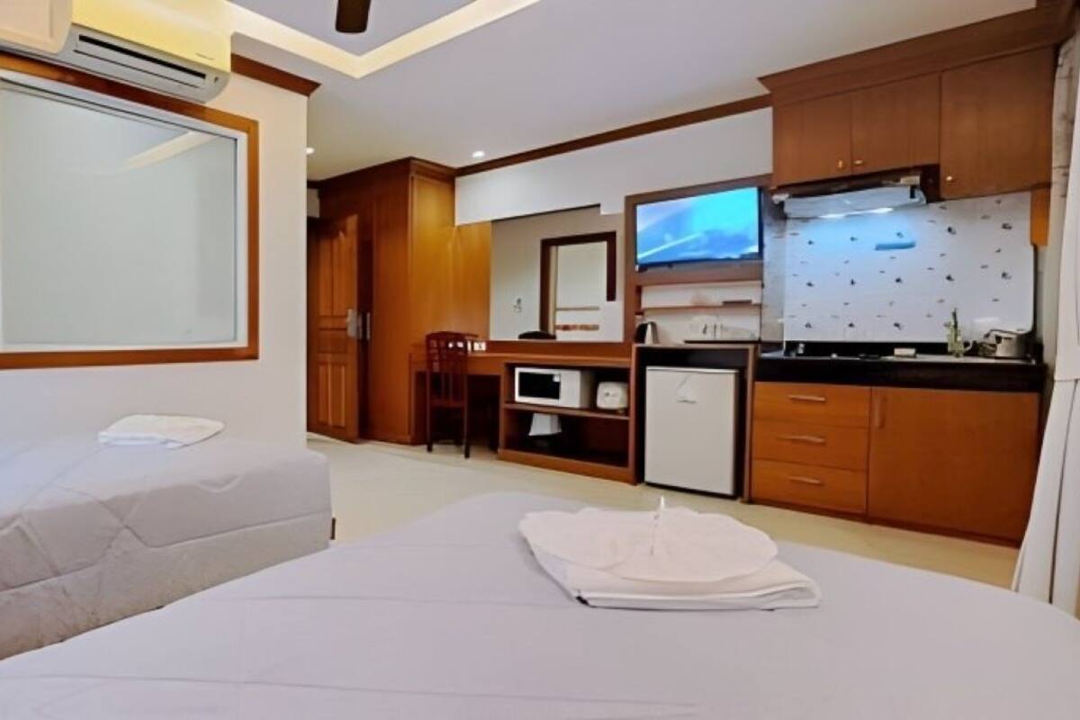 A hotel room with two beds, a kitchenette, a dining area, and a large mirror.