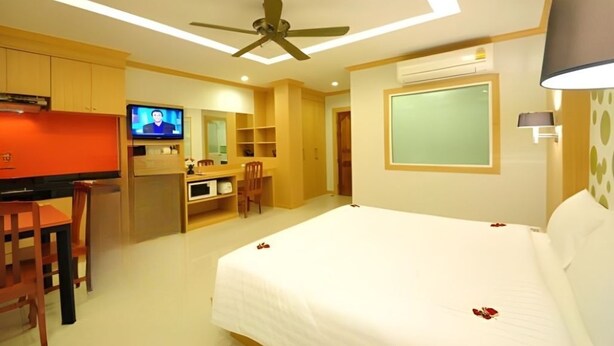 Una camera d'albergo con un letto, una scrivania, una televisione e una ventola a soffitto.