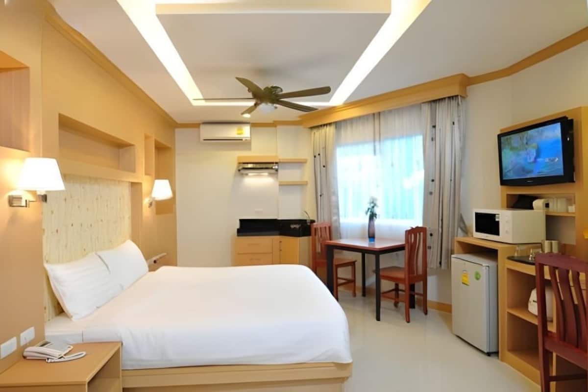 A hotel room with a bed, desk, chair, television, microwave, and a ceiling fan.