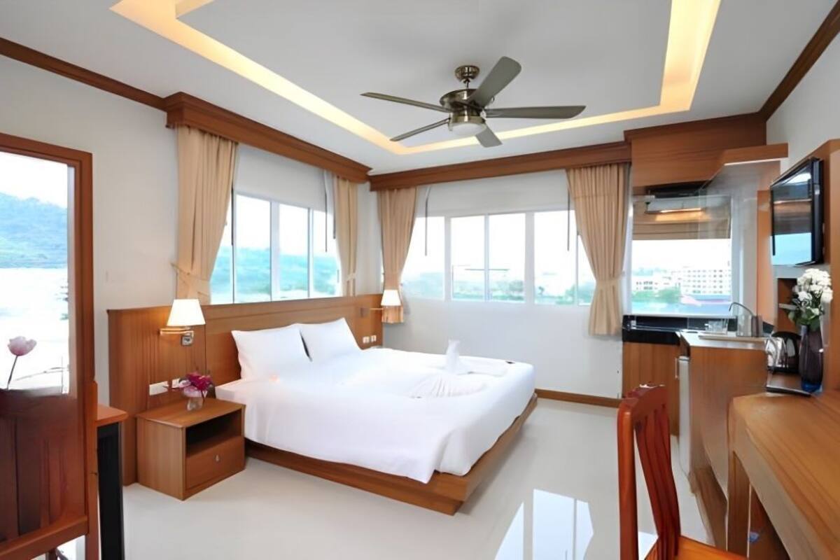 A hotel room with a bed, bedside table, lamp, TV, and a view of the outdoors.