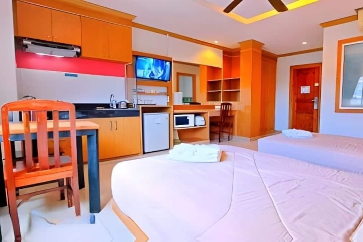 A hotel room with a bed, a desk with a chair, a television, a microwave, and a small kitchenette.