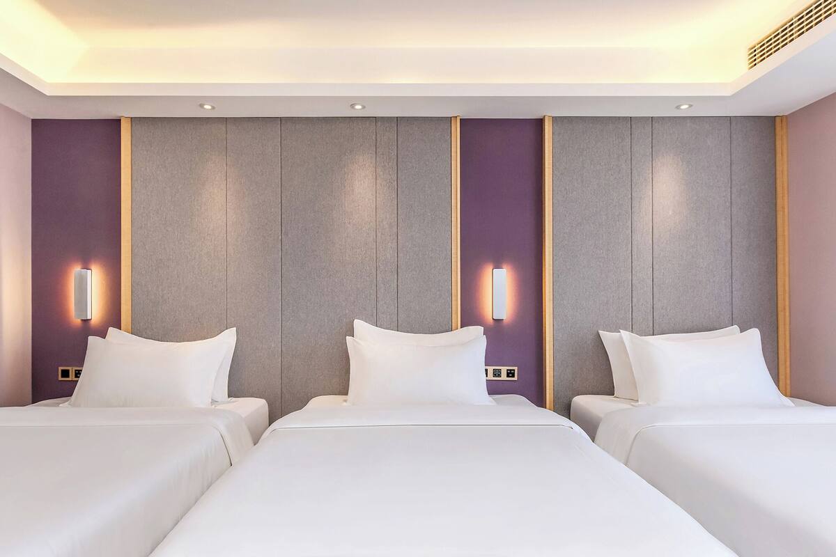 Ein Hotelzimmer mit drei Betten, modernem Design und integrierter Beleuchtung.