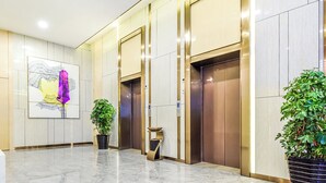 A modern lobby with marble flooring, two elevators, a large abstract painting, and potted plants. - Lavande Hotel Tianmenshan Branch (Zhangjiajie)