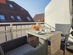 A balcony with wicker furniture, a table with breakfast items, and red-tiled roofs in the background. - Vacation apartment Sonnenschein - Holiday apartment Sonnenschein - Modern time-out for 2 (Norden)