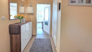 Un corridoio con un armadietto in legno, uno specchio, un vaso di fiori e una porta che dà su un'altra stanza.