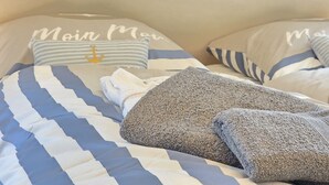 Un letto con lenzuola a righe e cuscini, un asciugamano piegato e un cuscino con motivo a ancora.