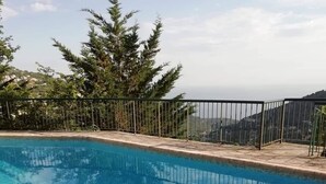 Piscina cristalina con valla metálica, rodeada de árboles y vistas a colinas distantes.