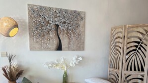 Un salón bien amoblado con un sofá, almohadones decorativos, un jarrón con flores, una obra de arte en la pared y un panel de pared texturizado.