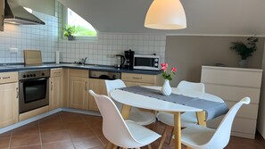 Une cuisine moderne avec un coin repas, comprenant une table blanche, des chaises et un vase rempli de fleurs.