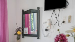 Une salle de bain avec un miroir, une commode, un vase à fleurs, un téléviseur fixé au mur et un téléphone.