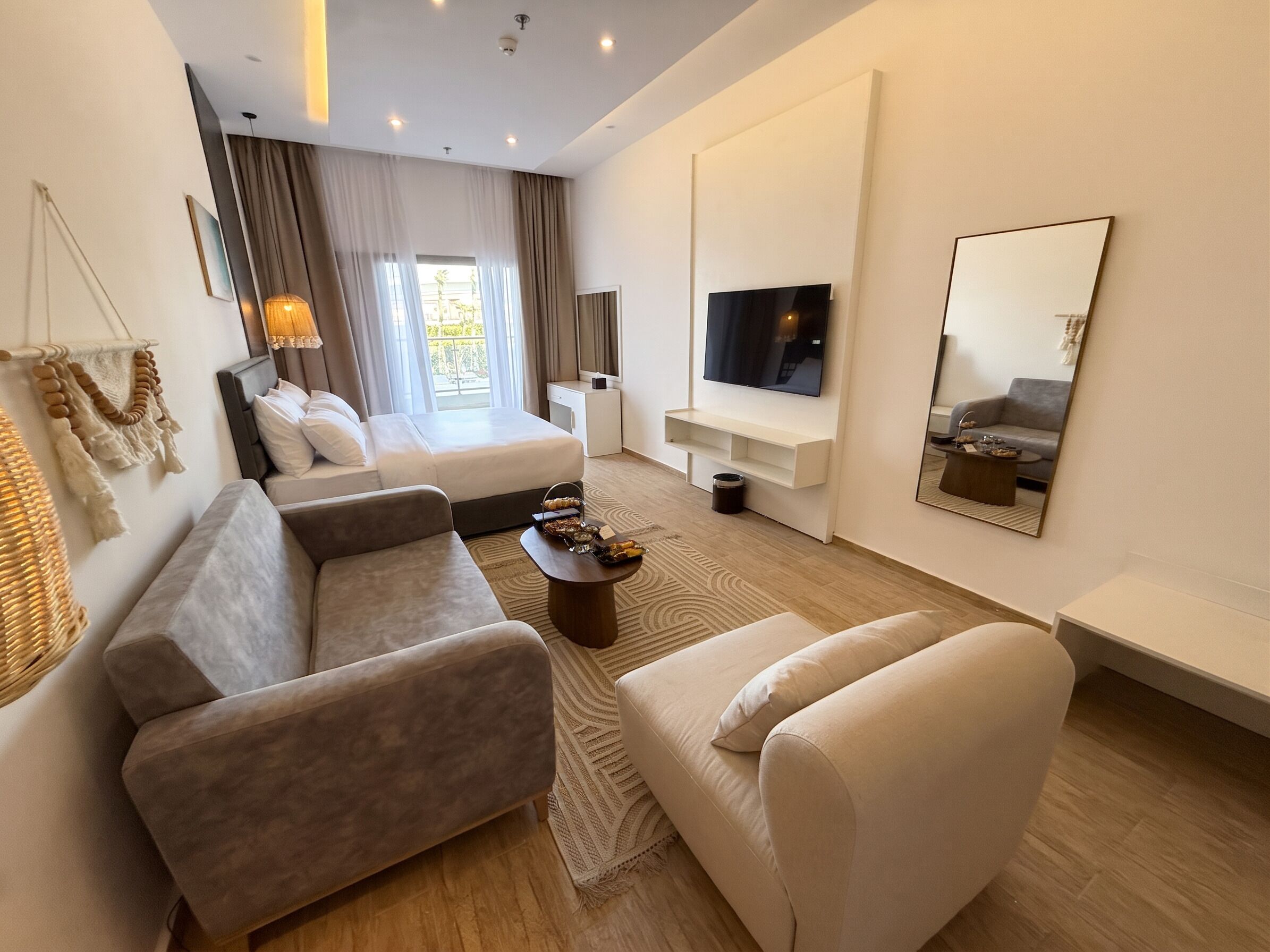 Una habitación de hotel moderna con una cama, dos sofás, un televisor y un espejo grande.