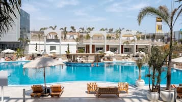 A pool area with lounge chairs and umbrellas, a clear sky, and a building with a sign reading 'Taga Arabia'.
