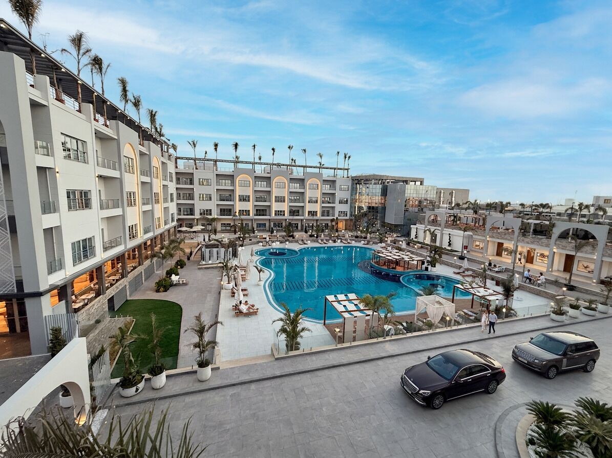 Un hotel con una amplia piscina exterior, varios balcones y un estacionamiento.