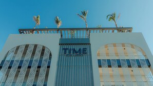 Un bâtiment doté d’une grande fenêtre en arc de cercle, d’un balcon orné de palmiers et du mot « TEMPS » inscrit sur la façade.