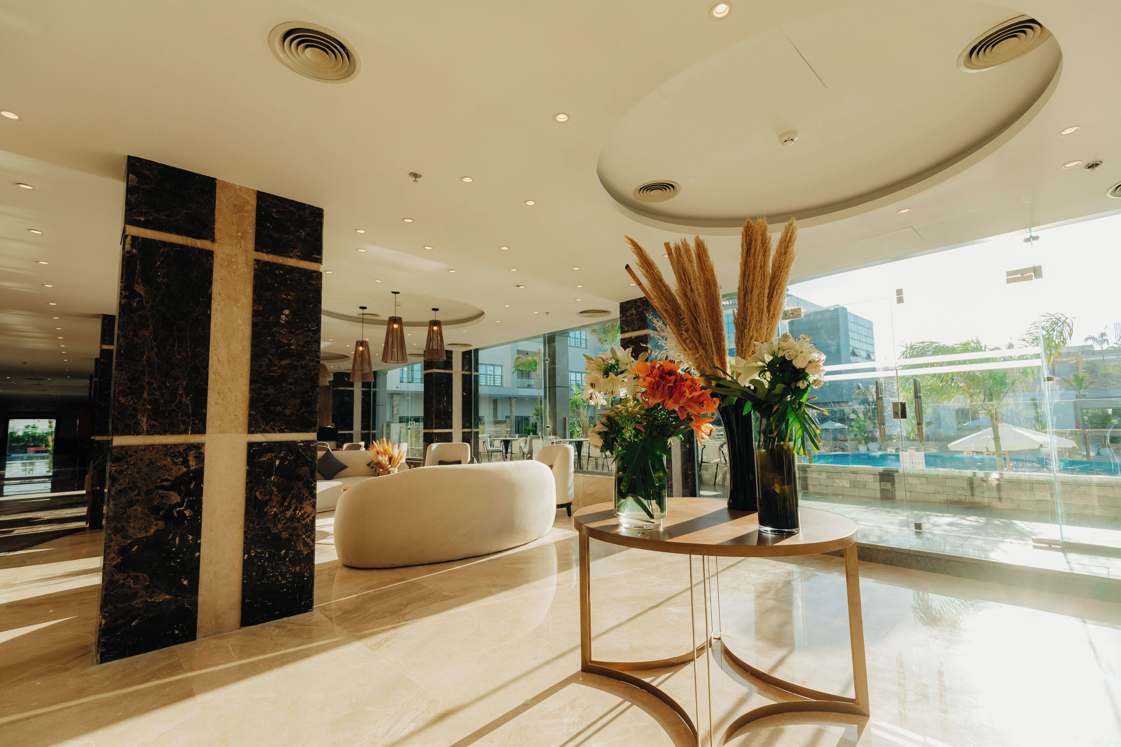 Eine moderne Lobby mit einer Marmorsäule, einem runden Tisch mit Blumen und einem großen Fenster mit Blick ins Freie.