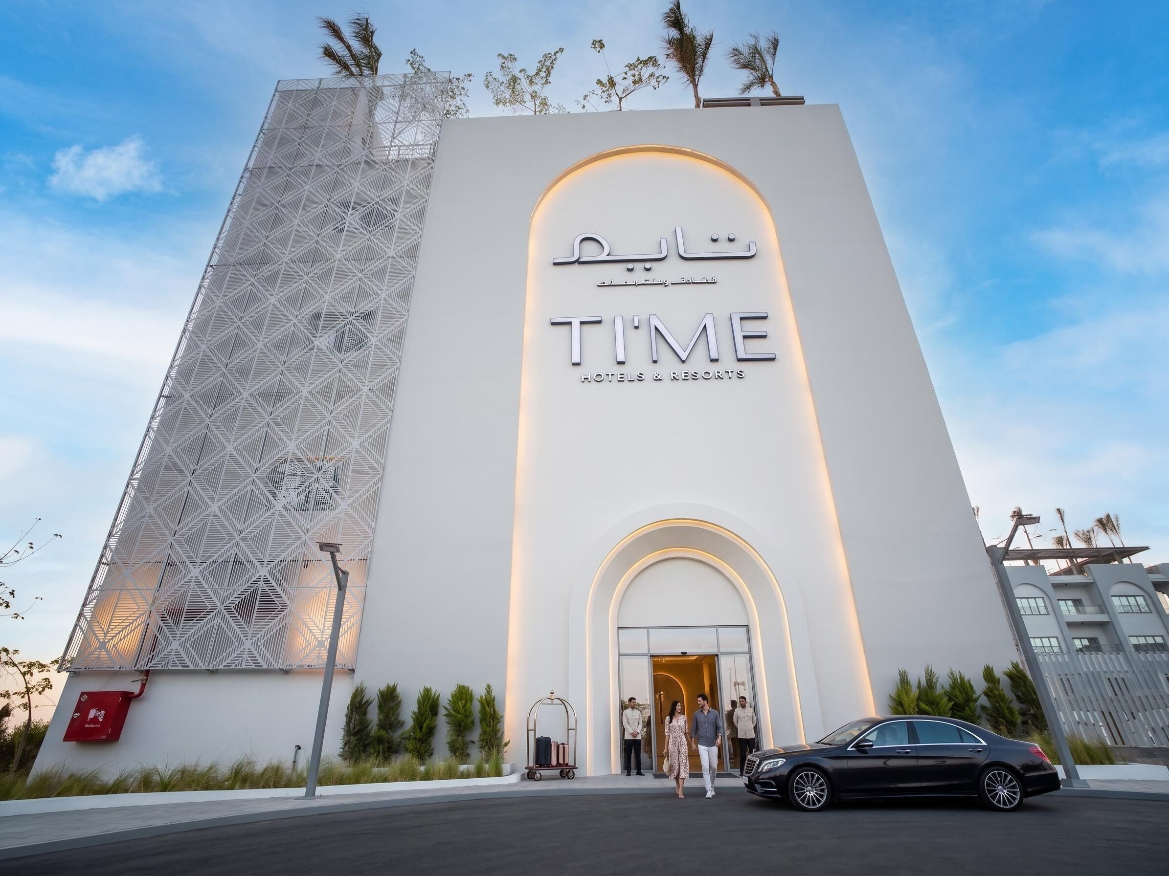 Une entrée d’hôtel moderne, dotée d’une façade géométrique et d’une enseigne indiquant « TIME Hotels & Resorts ».