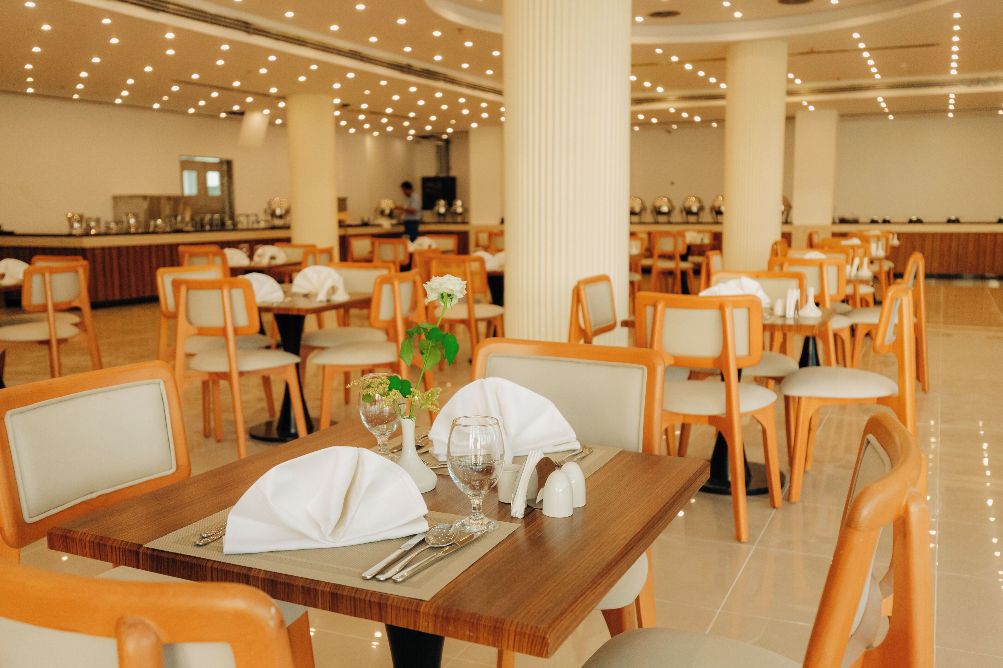 A restaurant with wooden tables and chairs, white napkins, and a central column.
