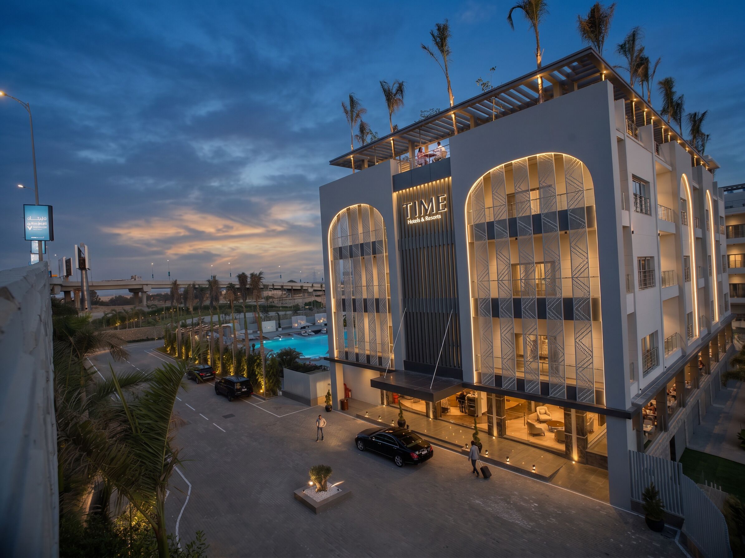 A hotel with a modern design, featuring a prominent entrance and a pool area.