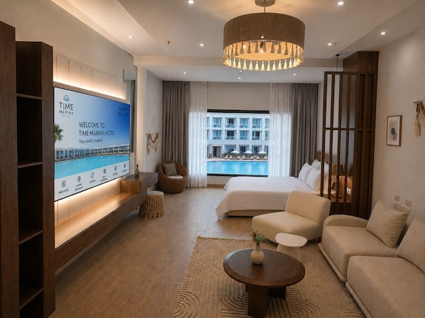 Une chambre d’hôtel moderne dotée d’une grande télévision, d’un lit, d’un canapé, d’une table basse et offrant une vue sur la façade de l’immeuble.