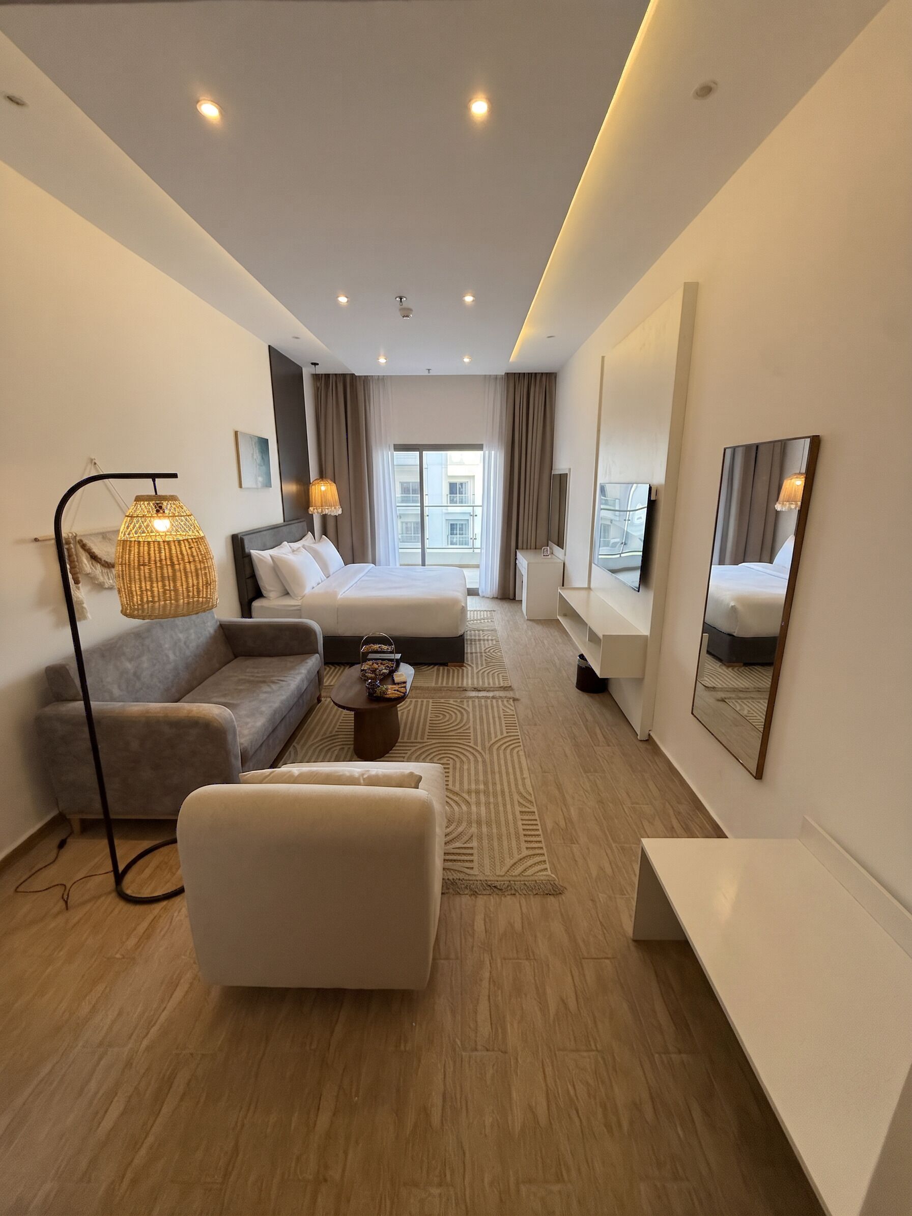 A modern hotel room with a bed, sofa, armchair, and a TV.