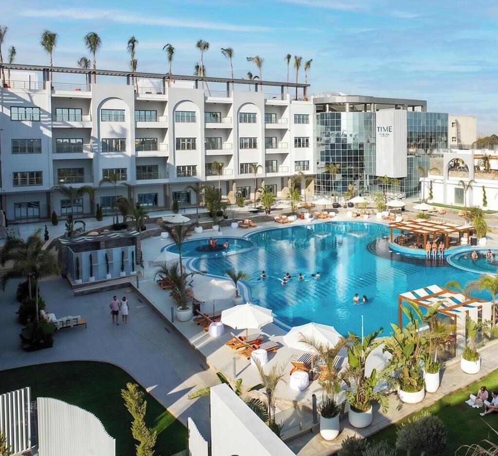 A hotel with a large swimming pool surrounded by lounge areas and palm trees.