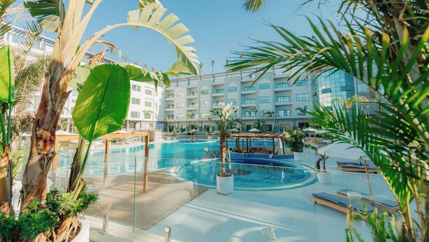 Un espace piscine d’hôtel comprenant une grande piscine, des chaises longues et des plantes tropicales.