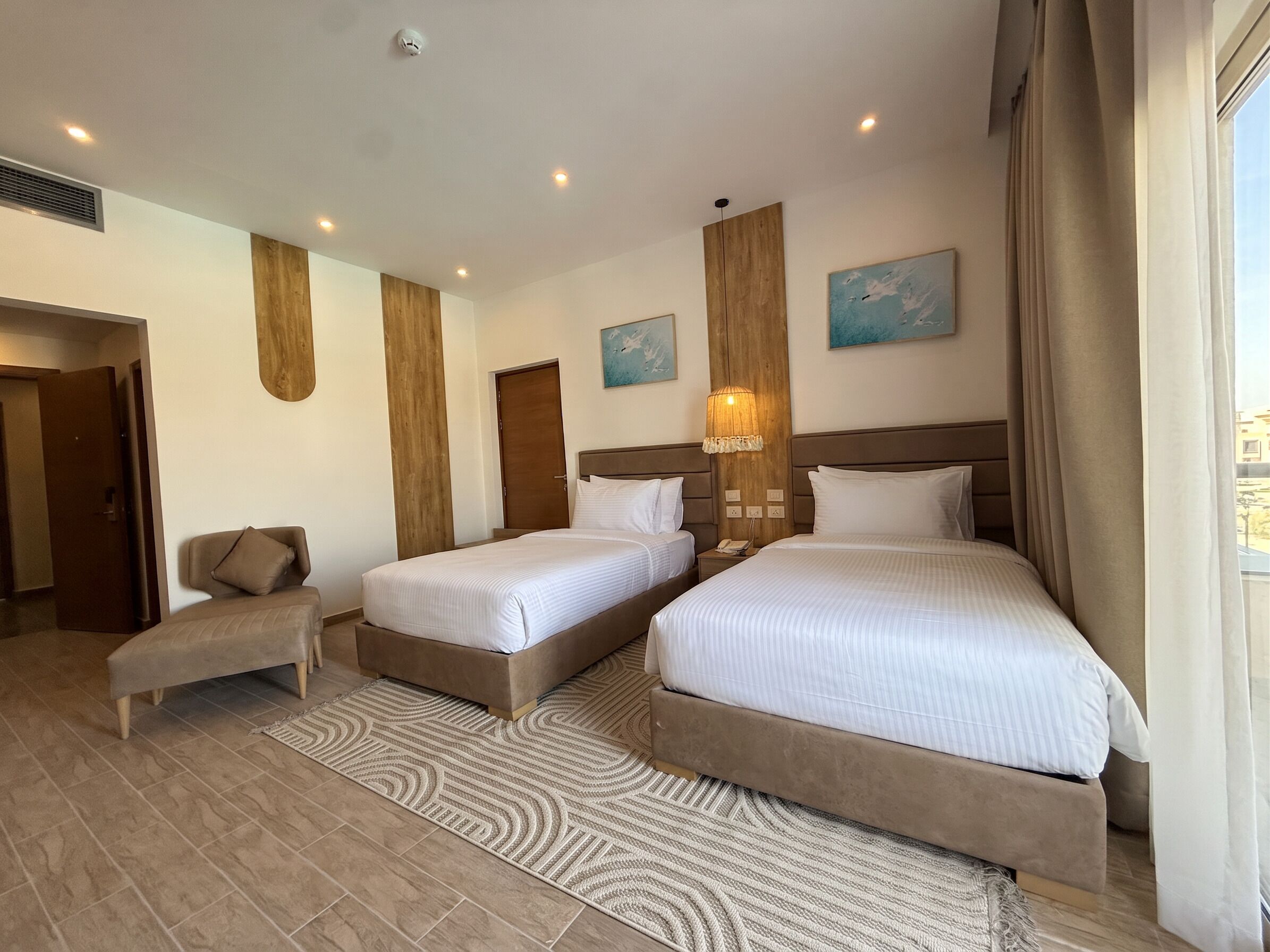 A hotel room with two beds, a sitting area, and a view of the outside.