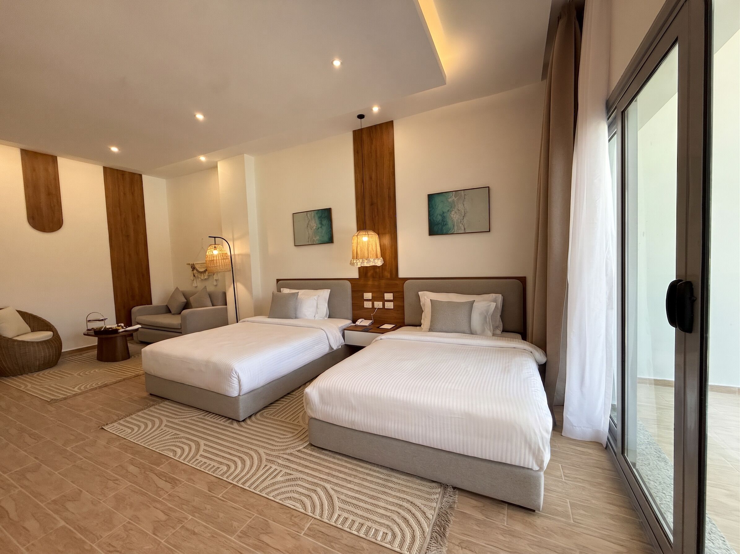 A hotel room with two beds, a sofa, a coffee table, and artwork on the walls.