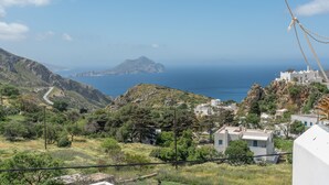 A coastal village with buildings, a winding road, and a view of the sea and distant island. - Room 6 at Pagali Hotel in Amorgos (Órmos Aiyialís)