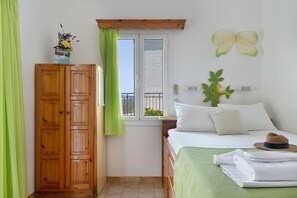 Un dormitori amb un armari de fusta, un llit amb roba de llit blanca, una cortina verda, una decoració de papallona i una finestra amb vistes.