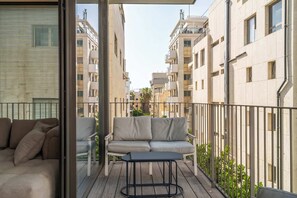A balcony with a sofa and table, surrounded by a metal railing, overlooking a row of buildings. - Bright 2BR Apartment Near Beach by HolyGuest (Tel Aviv-Yafo)