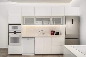 A modern kitchen with white cabinetry, a stainless steel refrigerator, a built-in oven, and a dishwasher. - Bright 2BR Apartment Near Beach by HolyGuest (Tel Aviv-Yafo)