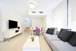 Ein modernes Wohnzimmer mit Flachbildfernseher, einer Couch, einem Couchtisch und einem Essbereich mit Stühlen und einem Tisch.